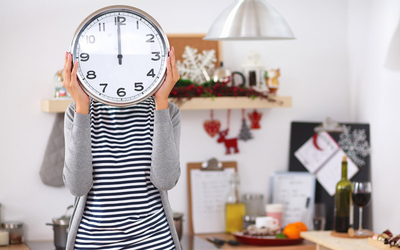 A woman standing in front of a kitchen area, holding a clock in front of her face