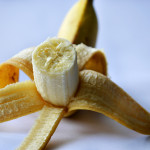 Banana on a white surface, peeled halfway open with the edible part facing the viewer