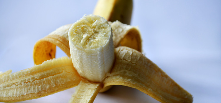 Banana on a white surface, peeled halfway open with the edible part facing the viewer