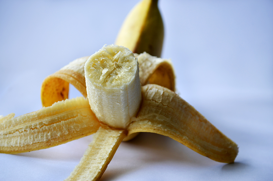 Banana on a white surface, peeled halfway open with the edible part facing the viewer