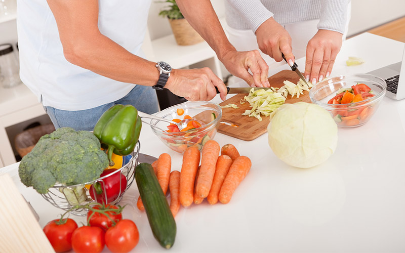 A food preparation area with a man and a woman working together to cut vegatables