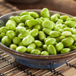 Edamame Beans in a brown ceramic bowl, placed upon a bamboo placemat