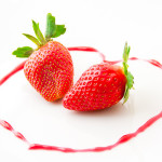 2 strawberries laying on a white surface, surrounded in a heart shaped line that has been drawn with strawberry juice