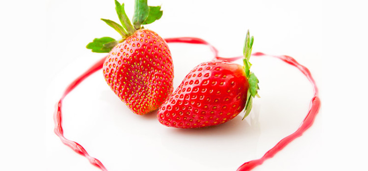 2 strawberries laying on a white surface, surrounded in a heart shaped line that has been drawn with strawberry juice