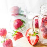 Sliced strawberries sprinkled around and in a glass mug that is filled with water