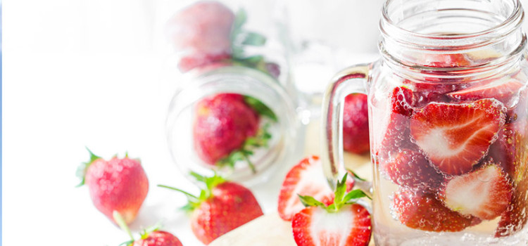 Sliced strawberries sprinkled around and in a glass mug that is filled with water