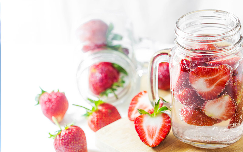 Sliced strawberries sprinkled around and in a glass mug that is filled with water