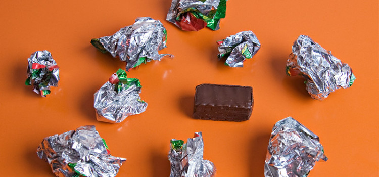 An orange surface with 9 crumpled silver candy wrappers and a single chocolate candy