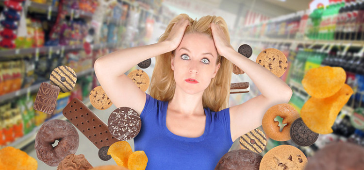 A harried looking woman in a blue t-shirt, grabbing clumps of her hair and staring at the viewer- surrounded by all forms of junk food that is flying around her.
