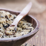 Mixed rice in a wooden bowl with a wooden spoon in it, all sitting on a rough wooden table top