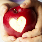 A childs hands holding an apple that has had a heart shaped bite taken out of it