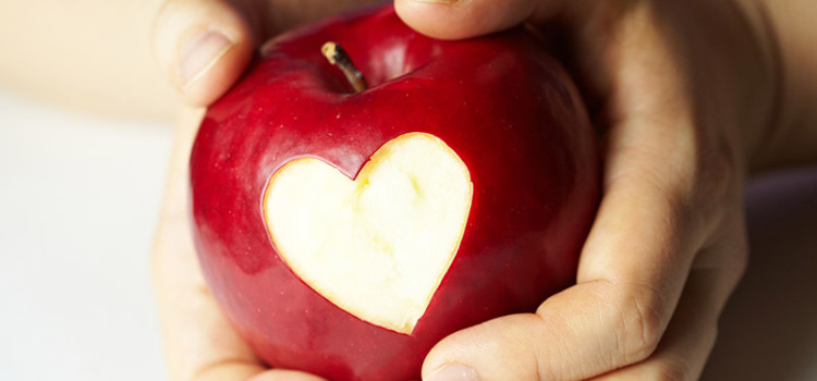 A childs hands holding an apple that has had a heart shaped bite taken out of it