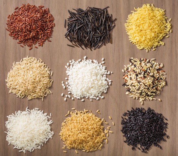 Piles of different rice varieties over a wooden background including jasmine basmati wild rice risotto and parboiled in Red white brown and black.
