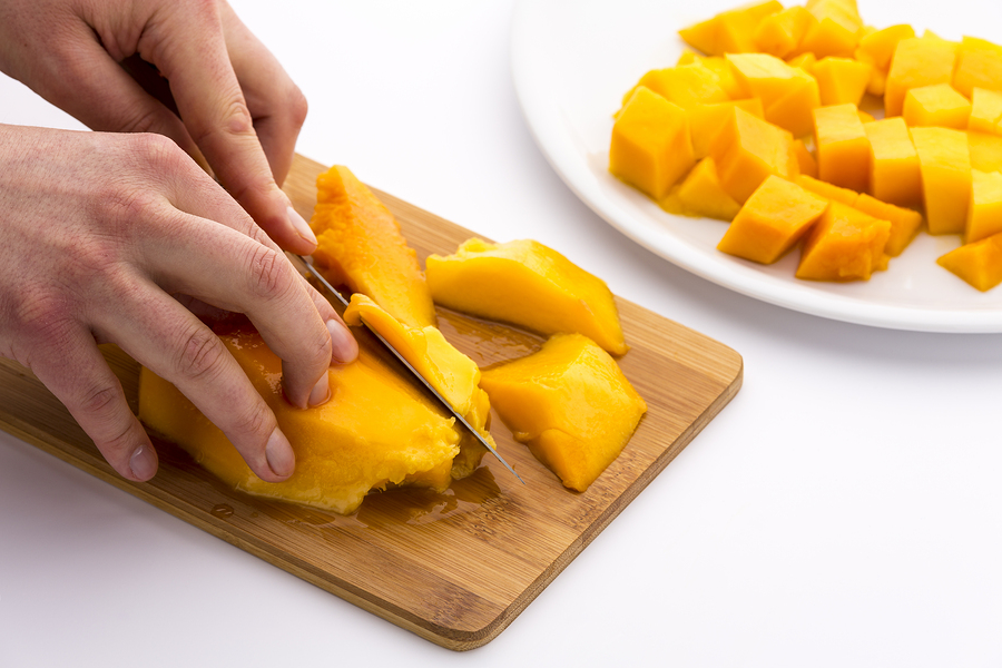 mango getting cut up- squared wedges in a white bowl by the side