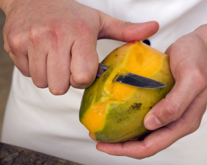 A man peeling the skin off a mango with a sharp knife