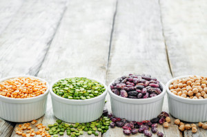 Variety of beans and lentils in small white cups on a wooden table top