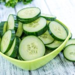 sliced cucumbers in a square green bowl on a wooden tabletop
