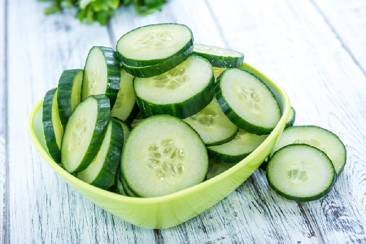 sliced cucumbers in a square green bowl on a wooden tabletop