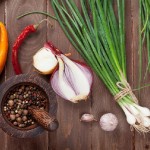 wooden table top with onions, peppers and other herbs and vegetables on it.