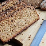 Slices of sprouted whole grain bread on a wooden cutting board with a bread knife in the foreground