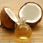 A coconut, cut in half, laying on a bambo mat with a glass jar of coconut oil in front of it.