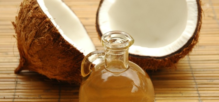 A coconut, cut in half, laying on a bambo mat with a glass jar of coconut oil in front of it.