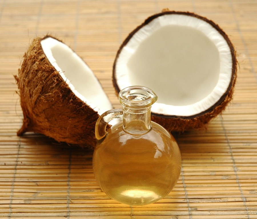 A coconut, cut in half, laying on a bambo mat with a glass jar of coconut oil in front of it.